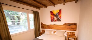 A bedroom with a wooden headboard, a bed with pillows, a window with curtains, and a painting on the wall.