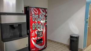 Ein Getränkeautomat mit verschiedenen Auswahlmöglichkeiten, ein Mülleimer und eine Tür in einem Flur.