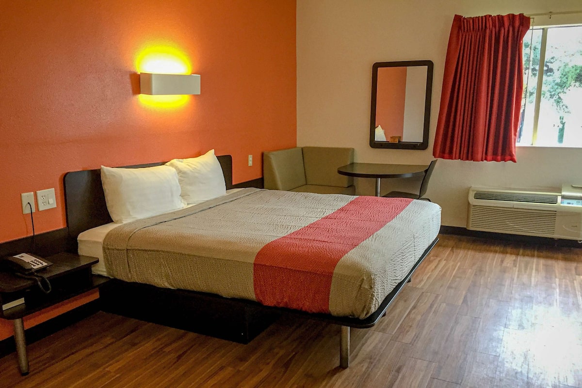 A hotel room with a bed, bedside table, chair, and a small table.