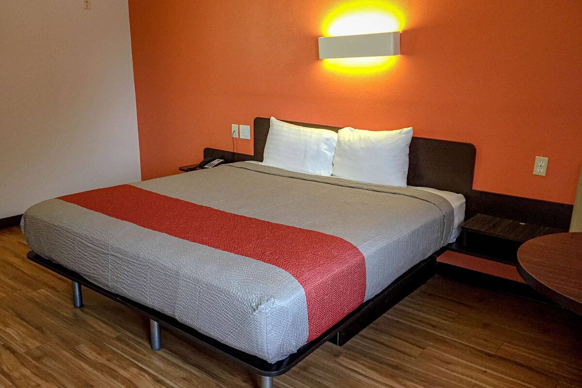 A hotel room with a bed, a bedside table, and a wall-mounted light fixture.
