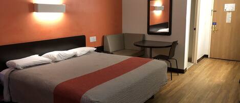 Une chambre d’hôtel avec un lit, une chaise, une petite table et une porte.