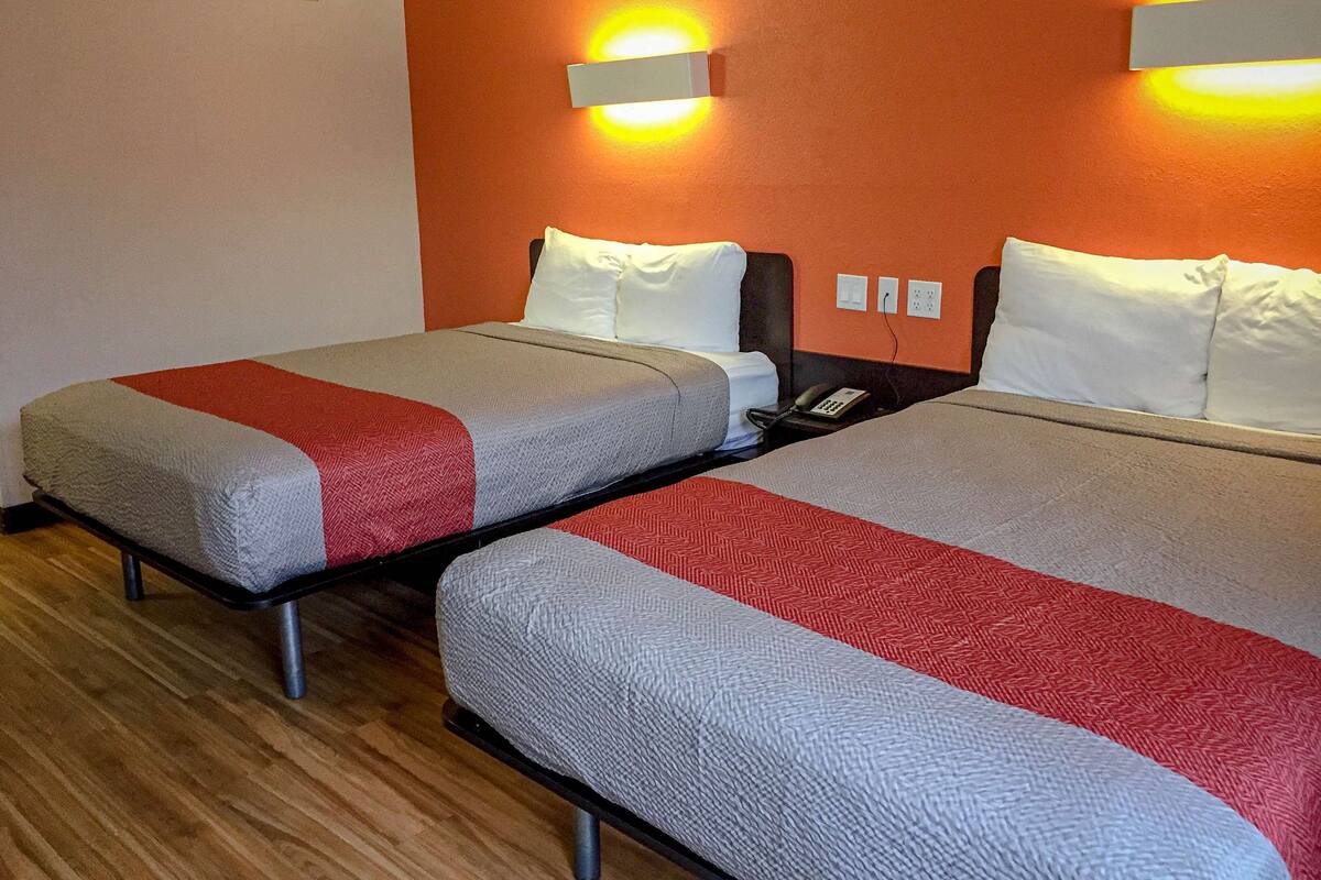 Two twin beds with grey and red bedding, a wooden floor, and a wall-mounted light fixture.