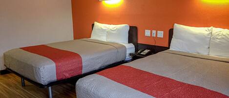 Two twin beds with grey and red bedding, a wooden floor, and a wall-mounted light fixture.