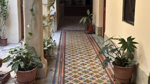A narrow corridor with tiled flooring, potted plants, and a patterned rug. - Hotel Margarita (Mérida)