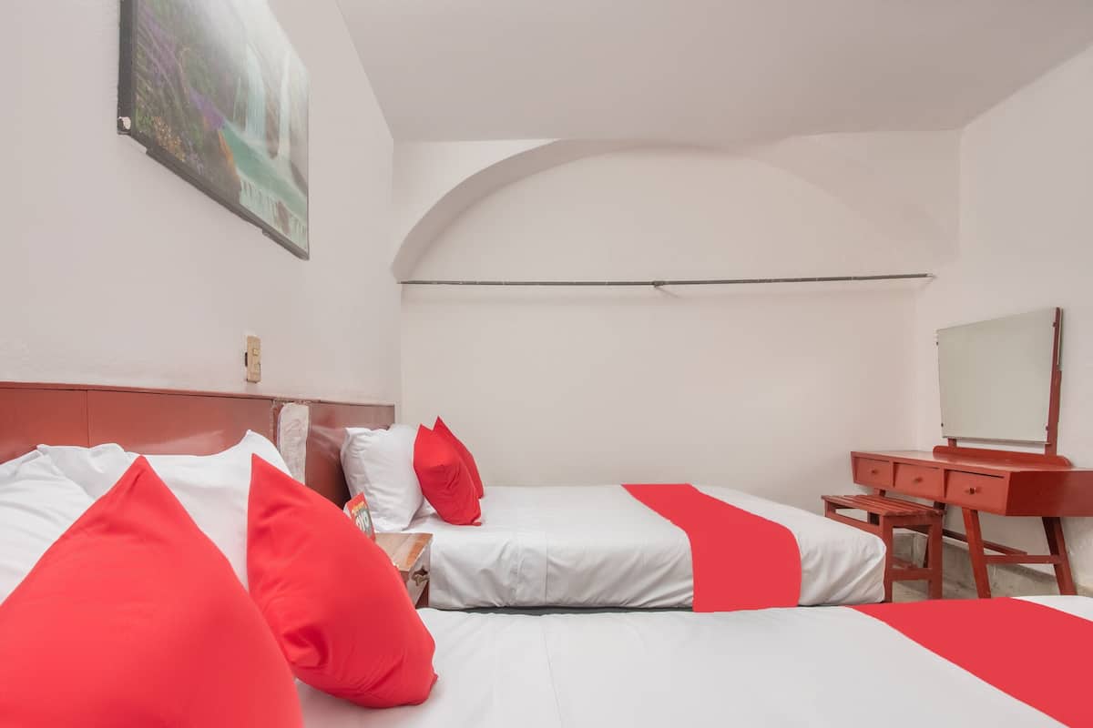 A hotel room with two beds, a desk, a mirror, and a painting on the wall.