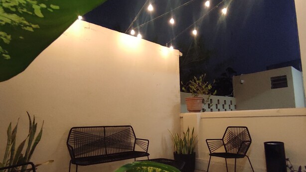 An outdoor patio area with two black metal chairs, a table, and potted plants. - Hotel Margarita (Mérida)