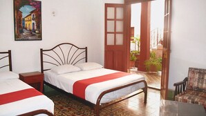 A bedroom with two beds, a wooden door, and a view of the outside. - Hotel Margarita (Mérida)