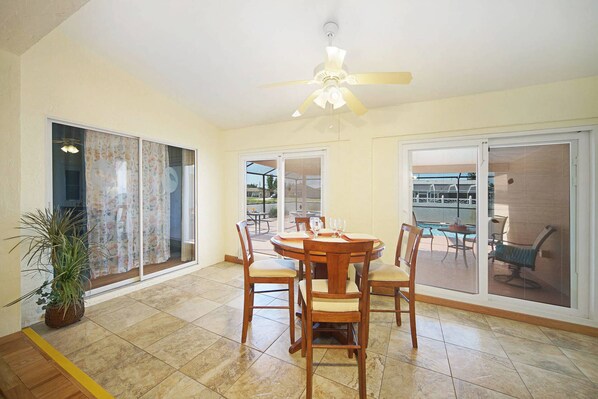 A spacious dining area with a round table and chairs, large windows, and a ceiling fan. - Pet Friendly Pool Home & Spa | Florida Room, Sleeps 8 | Southwest Cape Coral Near Sands Park (Cape Coral)