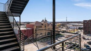 Vista desde un balcón con baranda metálica, sobre un estacionamiento y edificios, incluyendo una gran estructura con cúpula.