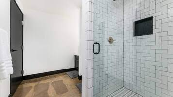 A modern bathroom with a glass shower enclosure, white tiled walls, and a wooden floor.