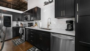 Una cocina moderna con gabinetes negros, electrodomésticos de acero inoxidable y un salpicadero de azulejos blancos.