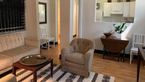 Uma sala de estar com sofá, poltrona, mesinha de centro e um espaço de jantar com mesa e cadeiras.