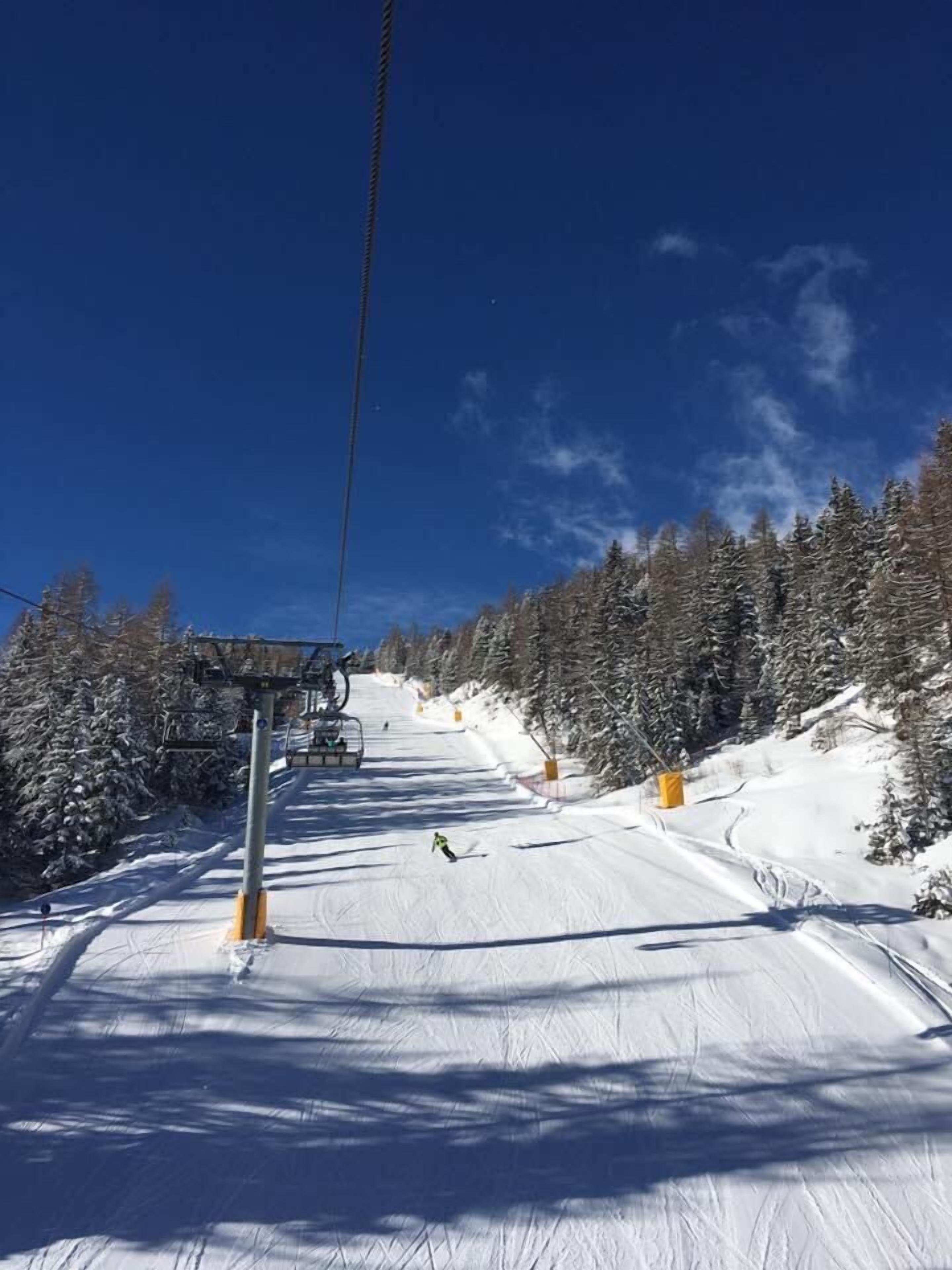Een skigebied met een stoeltjeslift en een besneeuwde helling met bomen.