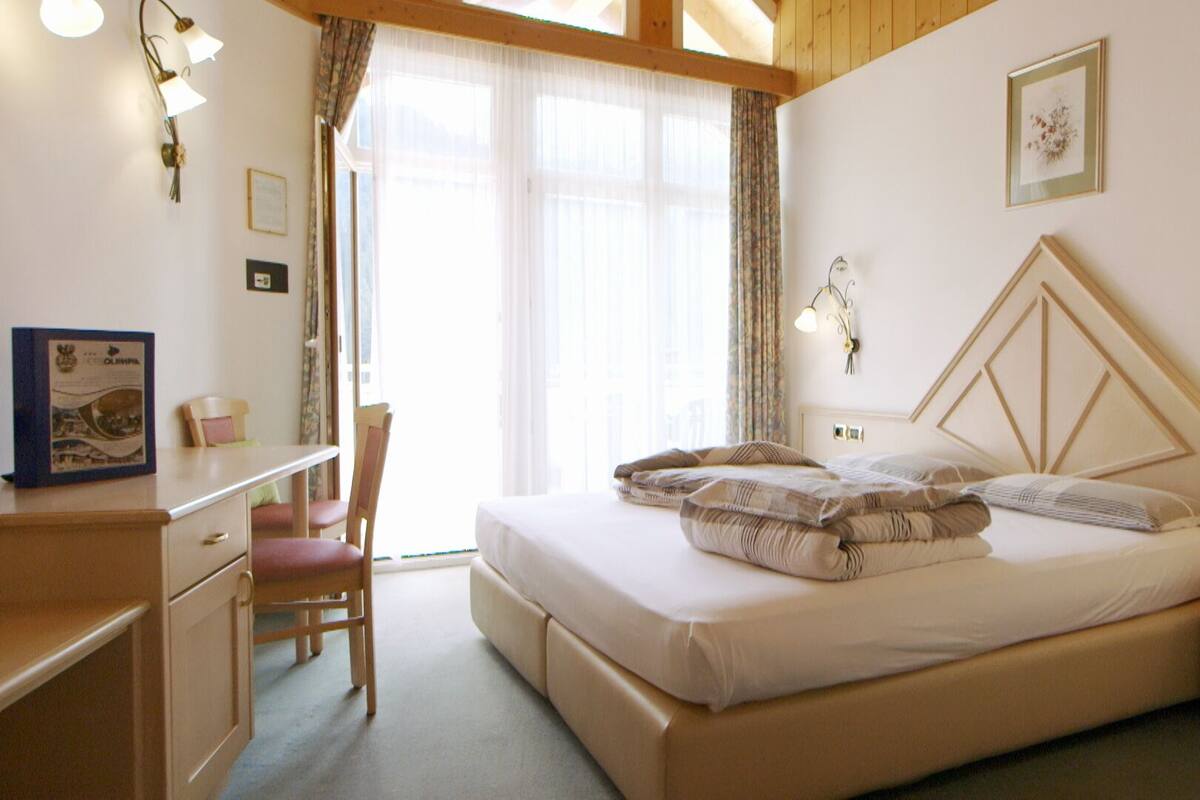 Ein Schlafzimmer mit einem Bett, einem Schreibtisch, einem Stuhl und einem Fenster mit Vorhängen.