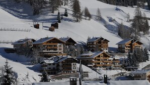 A snow-covered mountain resort with multiple wooden buildings, ski slopes, and snow-covered trees. - Hotel Olympia (Livinallongo del Col di Lana)