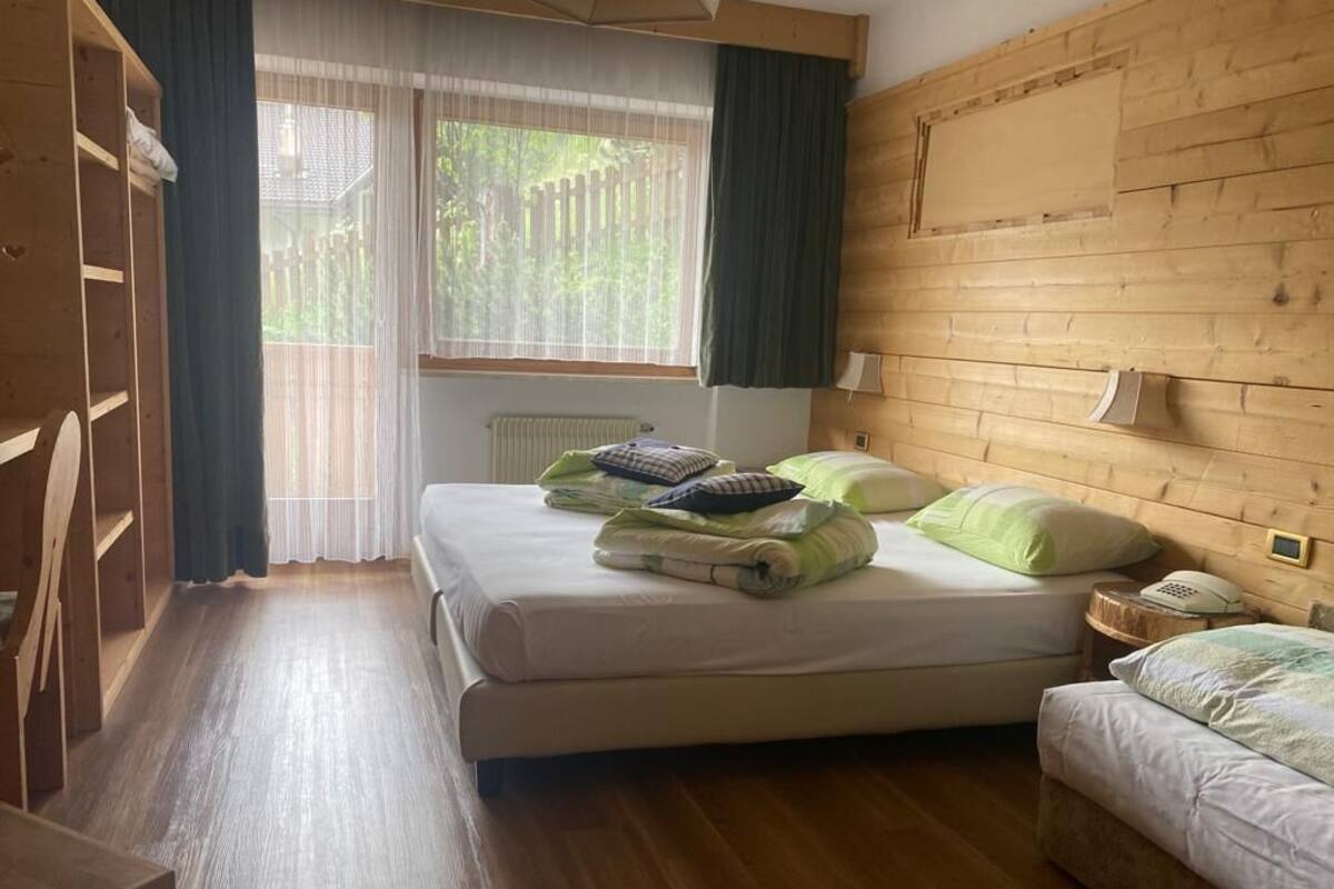 Ein Schlafzimmer mit einem hölzernen Kopfteil, einem Bett mit Kissen, einem Nachttisch mit Lampe und einem Fenster mit Vorhängen.