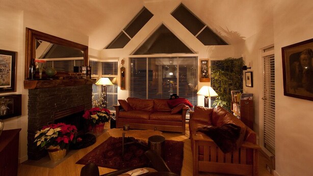 Una sala de estar acogedora con chimenea, sofás de cuero y un gran ventanal con persianas.