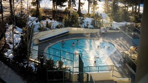 Un área de piscina con una piscina circular, rodeada de terreno y árboles cubiertos de nieve.
