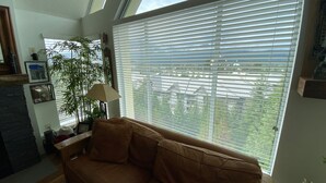 Una sala de estar con un sofá marrón, una lámpara, una planta en maceta y un ventanal con persianas.