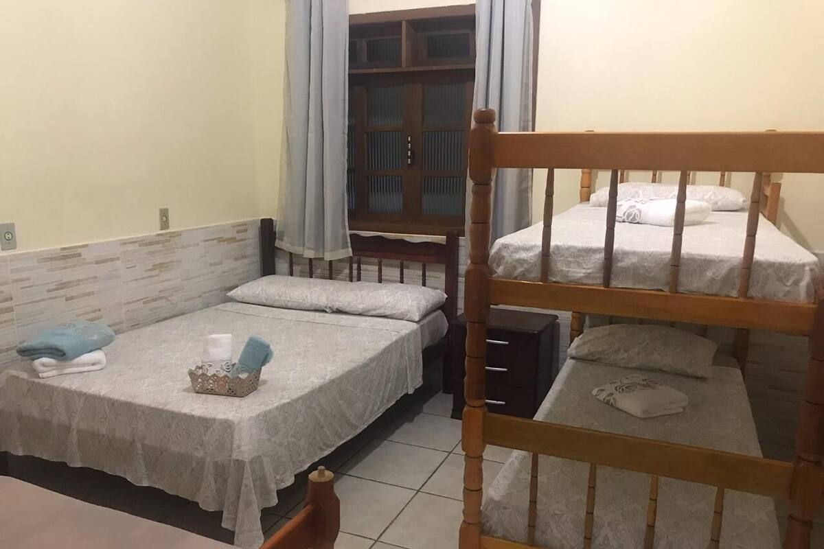 A dormitory room with two single beds, a wooden bunk bed, a small table, and a window with curtains.