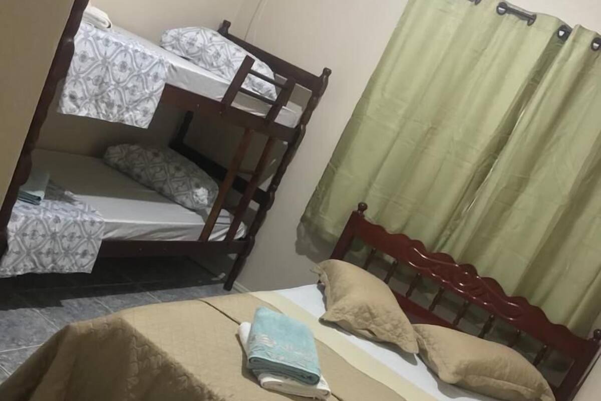 A small, compact room with a bunk bed and a single bed. The room has a tiled floor and a curtain on the window.