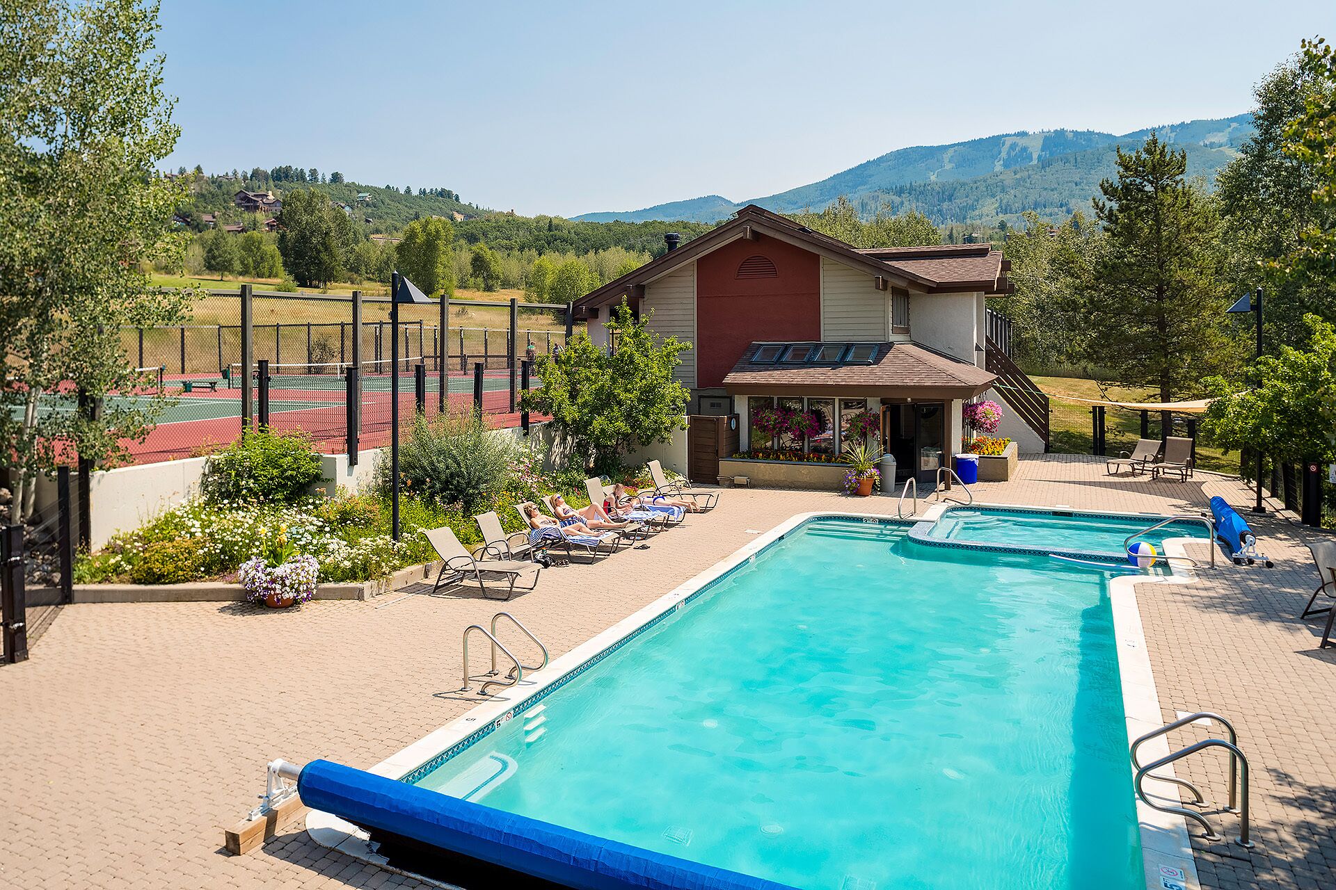 A pool area with two pools, lounge chairs, and a tennis court.
