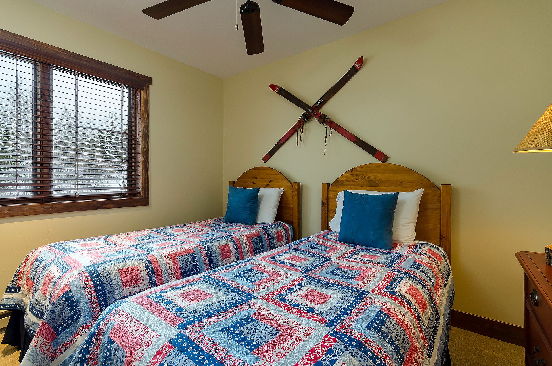 A bedroom with two beds, wooden headboards, and a window with blinds.