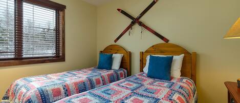A bedroom with two beds, wooden headboards, and a window with blinds.