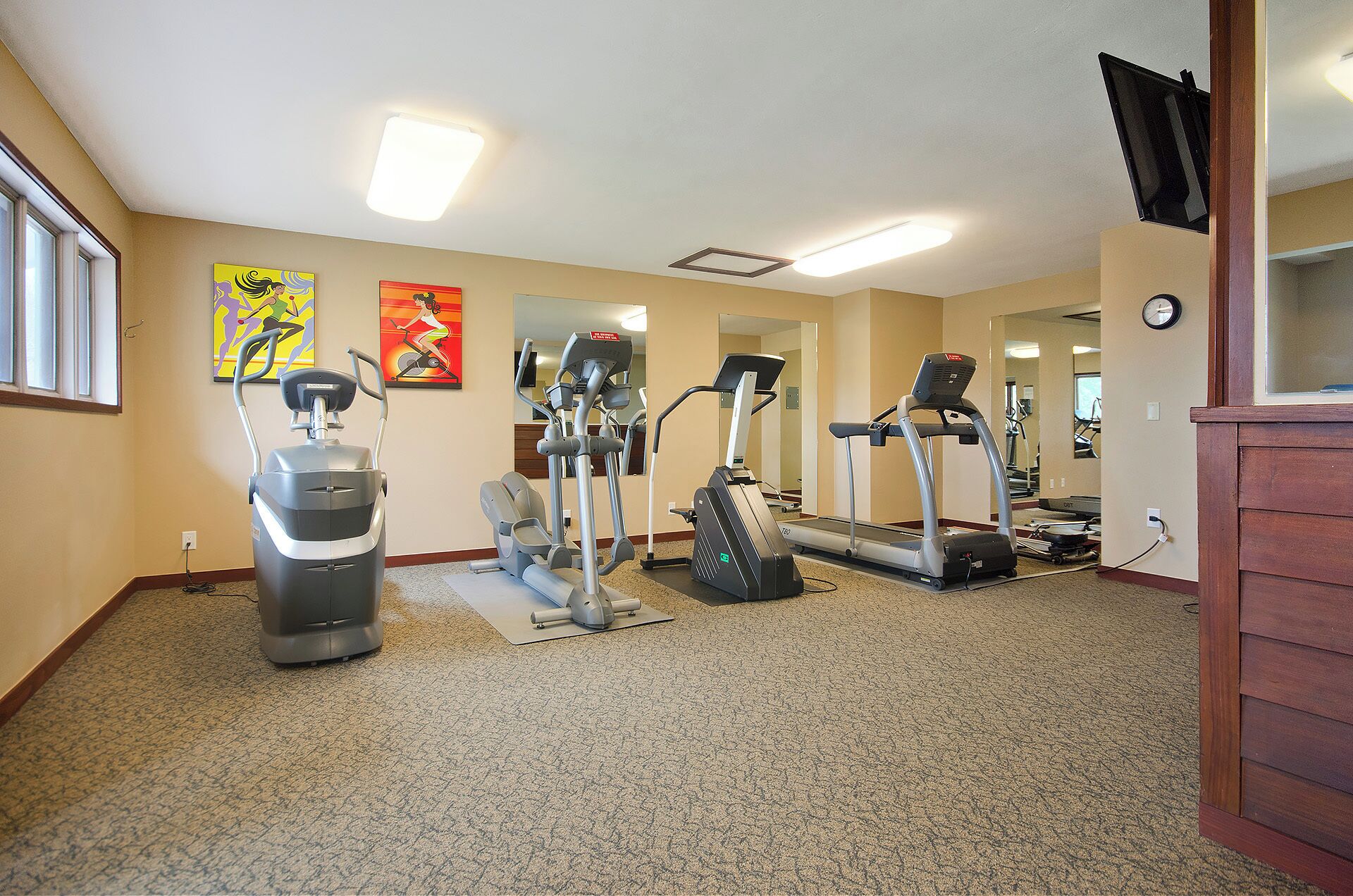 A fitness room with cardio machines, a mirror, and artwork on the walls.