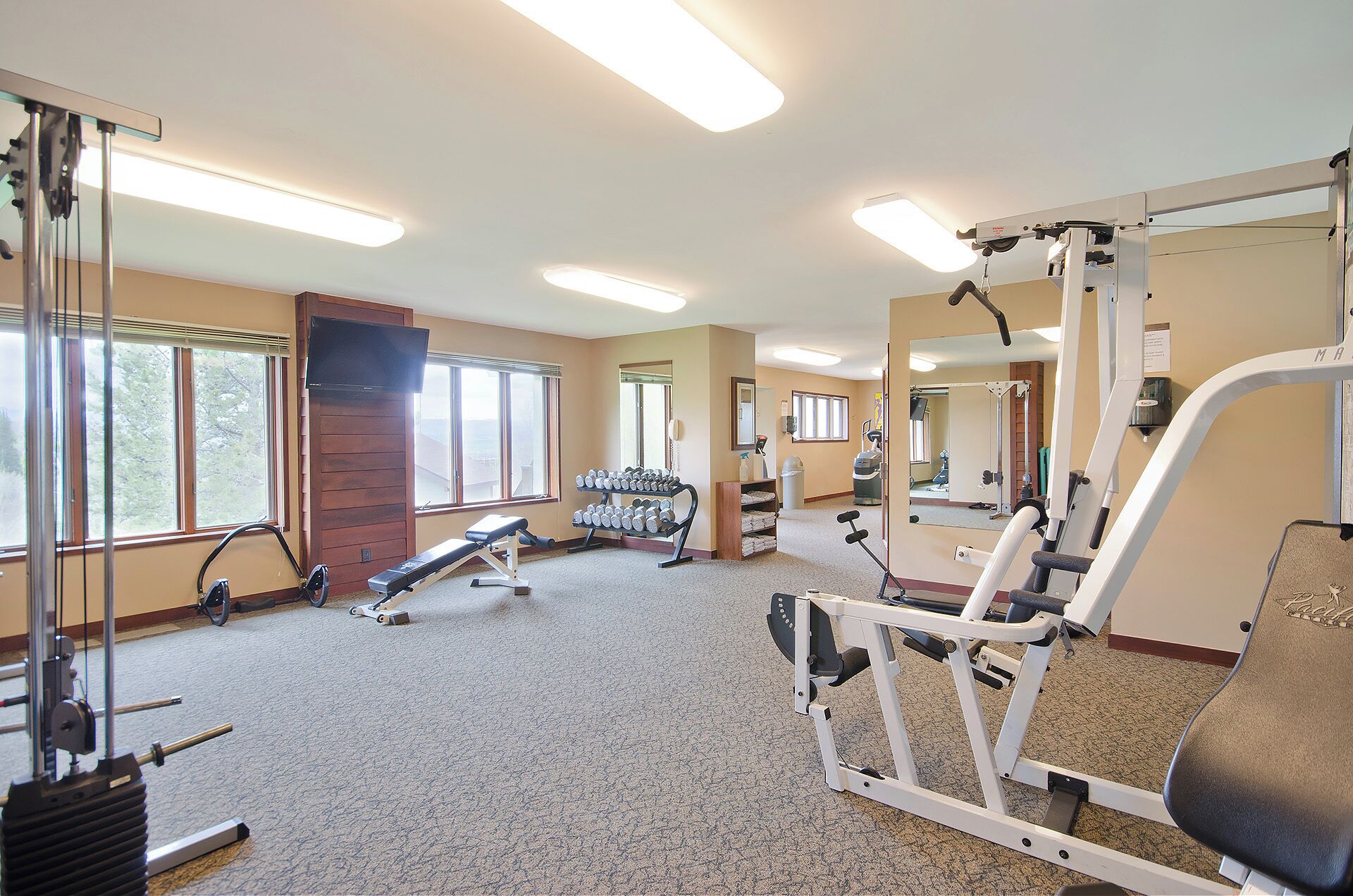 A gym with various exercise equipment, large windows, and a mirror.
