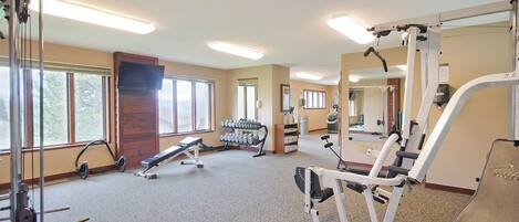 A gym with various exercise equipment, large windows, and a mirror.
