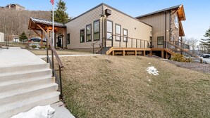 A two-story building with a covered porch, a flagpole, and a staircase leading to the entrance. - Lovely ski-in/out condo with gorgeous mountain views and shared tennis court (Sugar Mountain)