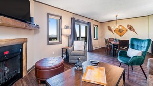 A living room with a fireplace, a dining area, and a chandelier. - Lovely ski-in/out condo with gorgeous mountain views and shared tennis court (Sugar Mountain)