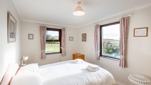 A bedroom with two beds, a wooden cabinet, a radiator, and a view of the outdoors.