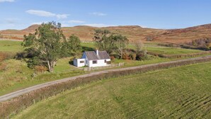 A white house with a blue roof surrounded by green fields and hills.
