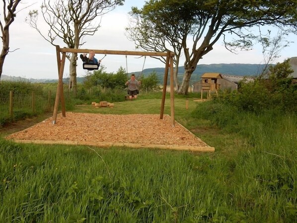 Een houten schommel met een uitzicht over het omliggende landschap, gelegen in een grasveld.