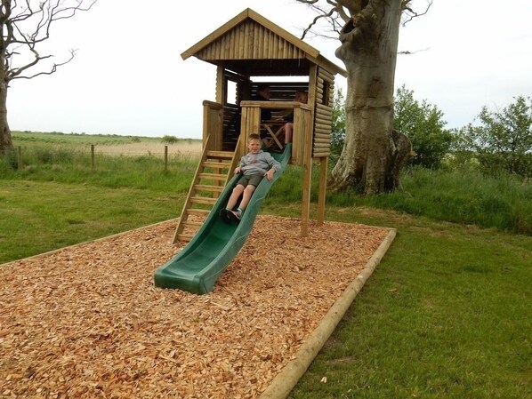 Een houten speeltoestel met een glijbaan en een klein, afgesloten klimgedeelte.