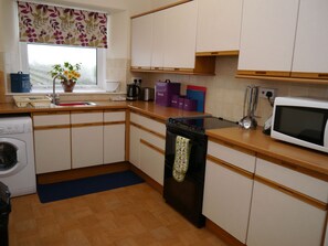 Een compacte keuken met houten kastjes, een inbouwoven, een magnetron en een raam met een bloemen gordijn.