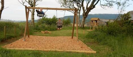 A wooden swing set in a grassy area with a clear view of the surrounding landscape.