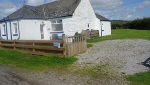 A white building with a grey roof, a wooden fence, and a gravel driveway. - Barnacle -  a cottage that sleeps 4 guests  in 2 bedrooms (Southwick-Sandyhills)