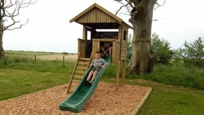 A wooden play structure with a slide and a small enclosed area for climbing. - Barnacle -  a cottage that sleeps 4 guests  in 2 bedrooms (Southwick-Sandyhills)