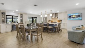 Une cuisine spacieuse comprenant un coin repas, un bar et un espace détente avec un téléviseur diffusant des images de « Roelens Vacations ».