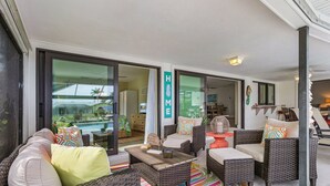 Un vaste espace de vie agrémenté de meubles en osier, d’un tapis rayé aux couleurs vives et offrant une vue sur une piscine et un espace extérieur.