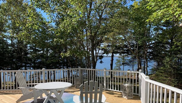 Une terrasse en bois avec une balustrade blanche, une table ronde et deux chaises Adirondack.