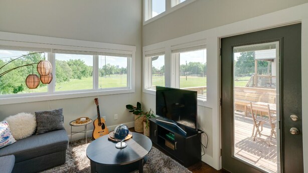 A living room with a sofa, coffee table, guitar, TV, and large windows overlooking a deck. - Perfect Downtown Views for the 4th of JULY / Watch FIREWORKS from private deck (Nashville)
