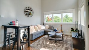 A modern living room with a grey sofa, a round coffee table, and a dining area with stools. - Perfect Downtown Views for the 4th of JULY / Watch FIREWORKS from private deck (Nashville)