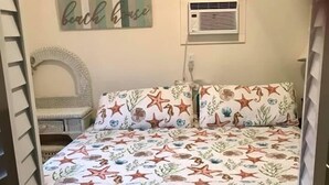 A bedroom with a bed featuring a sea-themed bedspread, a wall-mounted air conditioner, and a decorative sign above the bed. - JJB Cabins (Matagorda)