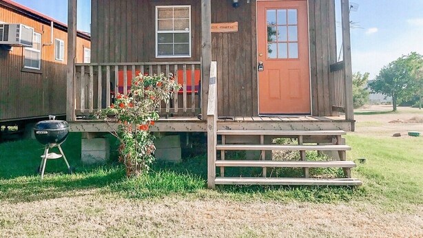 A wooden cabin with a red door, a small porch, and a star emblem on the roof. - JJB Cabins (Matagorda)