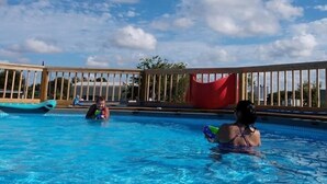 A swimming pool with clear blue water, surrounded by a wooden deck and a red canopy. - JJB Cabins (Matagorda)
