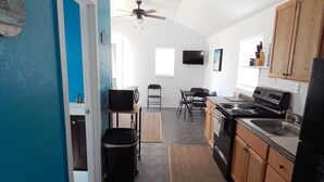 A kitchen with a microwave, stove, and sink. There is a ceiling fan, a dining table with chairs, and a small rug. - JJB Cabins (Matagorda)
